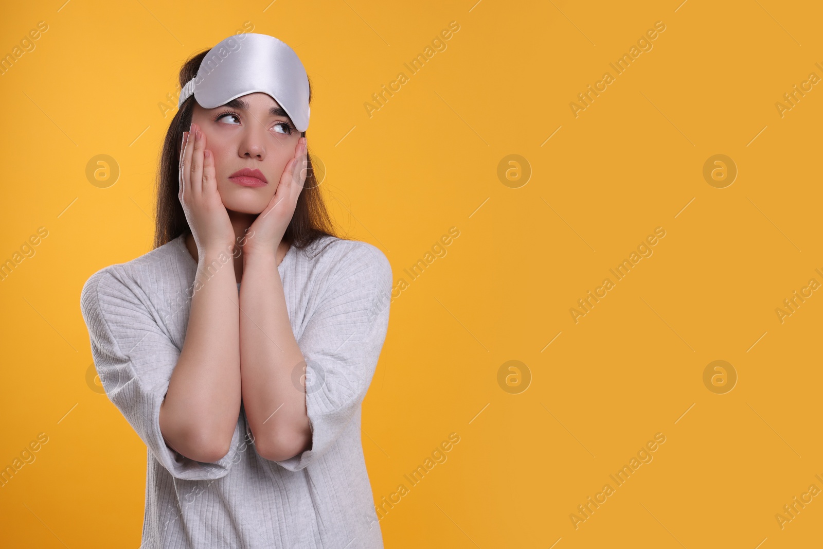 Photo of Tired young woman with sleep mask on yellow background, space for text. Insomnia problem