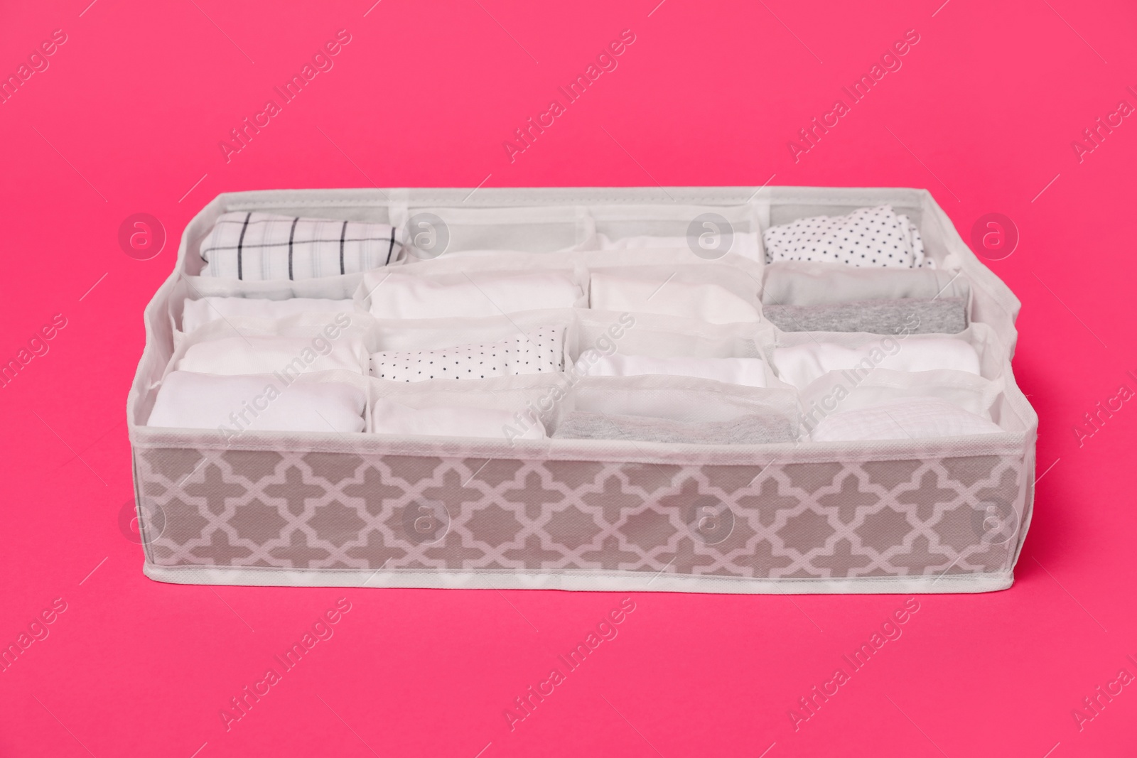 Photo of Textile organizer with folded clothes on pink background