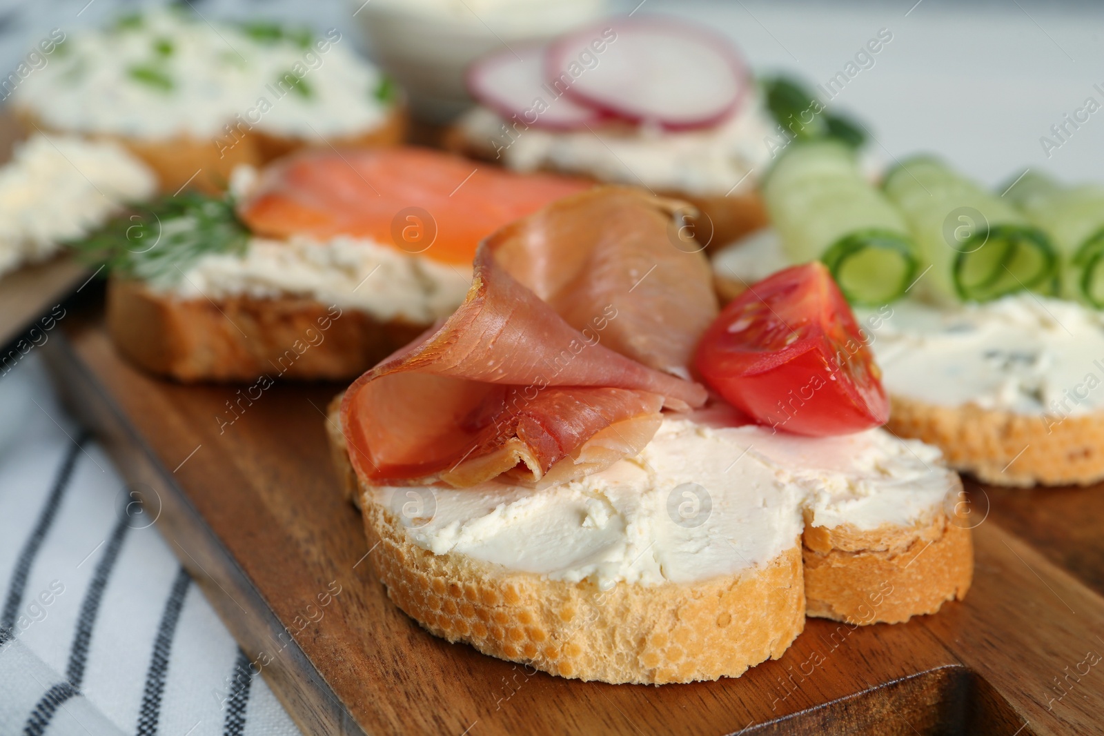 Photo of Toasted bread with cream cheese and different toppings on wooden board, closeup