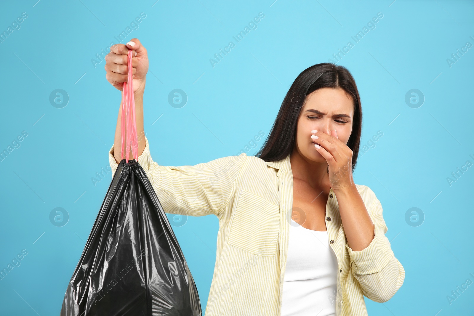 Photo of Woman holding full garbage bag on light blue background