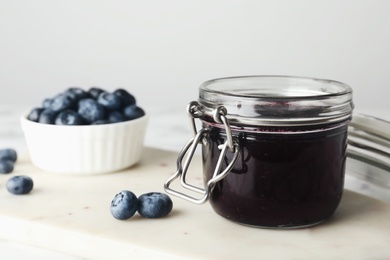 Jar of blueberry jam and fresh berries on table, closeup