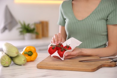 Photo of Woman wiping tomatoes with paper towel in kitchen, closeup