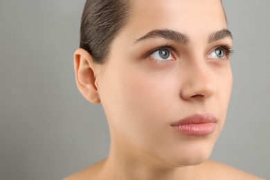 Photo of Young woman with perfect eyebrows on grey background, closeup