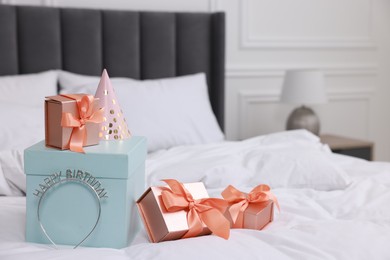 Photo of Many gift boxes, headband and party hat on bed in room. Happy Birthday