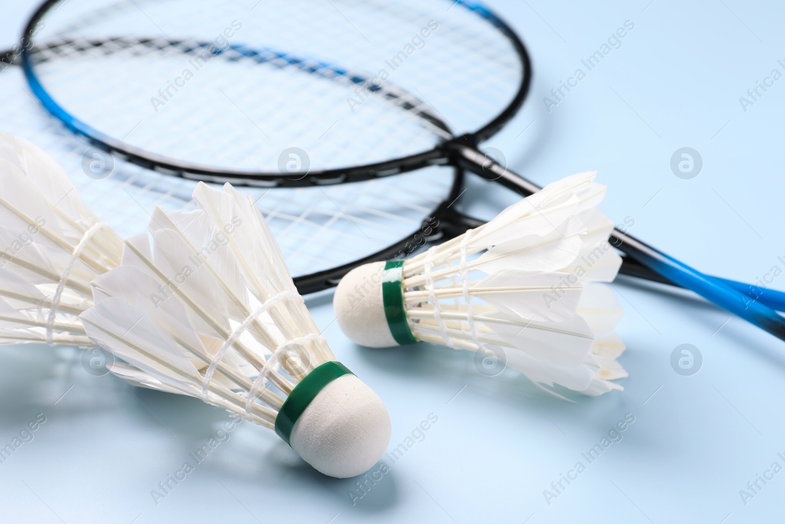 Photo of Feather badminton shuttlecocks and rackets on light blue background, closeup