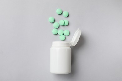 Photo of Light green vitamin pills and bottle on grey background, top view