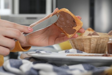 Woman spreading tasty nut butter onto toast indoors, closeup