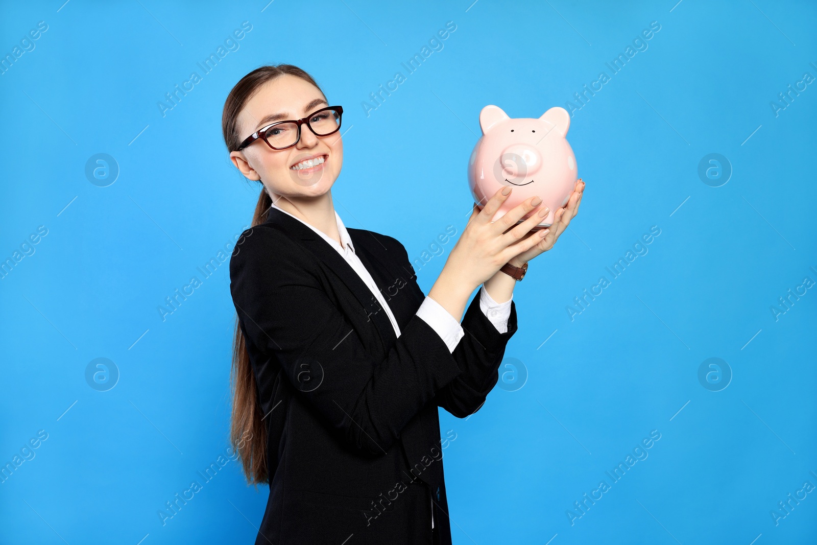 Photo of Happy young businesswoman with piggy bank on light blue background