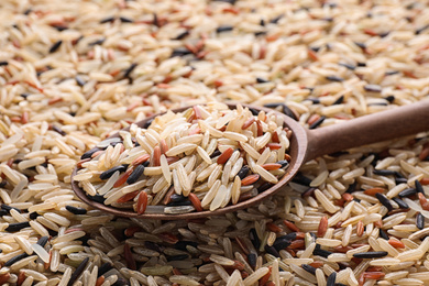 Photo of Mix of different brown rice and wooden spoon, closeup