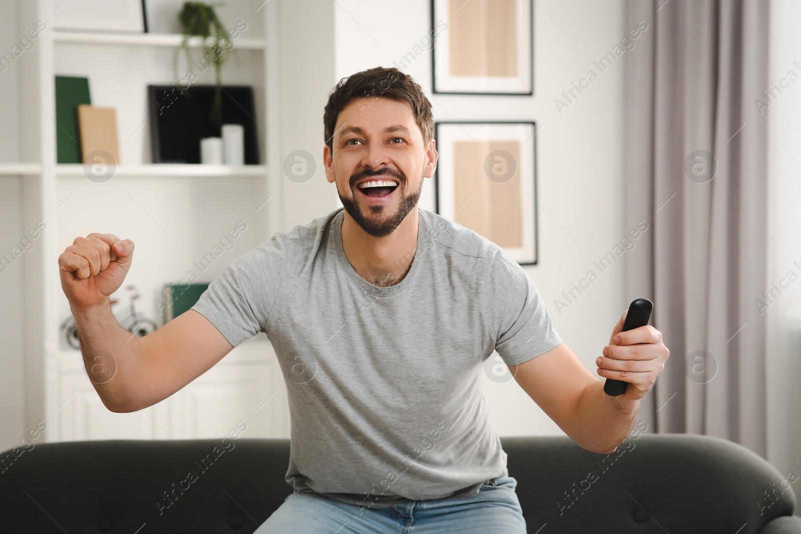 Photo of Emotional man holding remote controller and watching TV at home