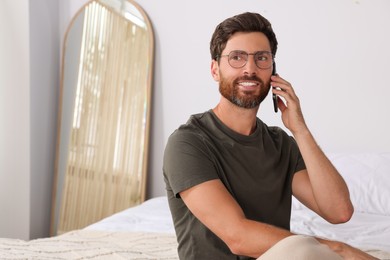 Handsome man talking on smartphone in bedroom, space for text