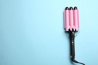 Photo of Modern triple curling hair iron on light blue background, top view. Space for text