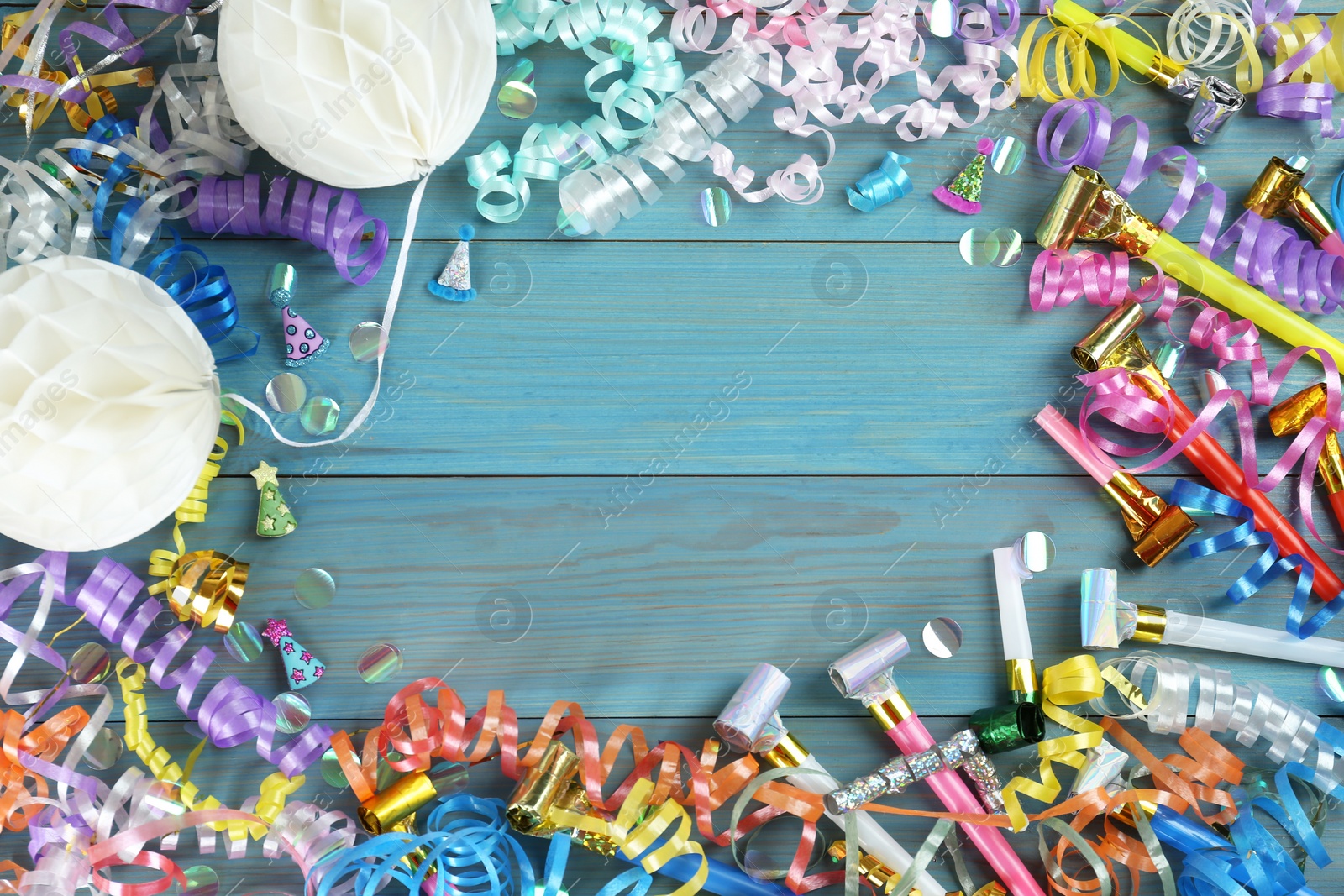 Photo of Frame of colorful serpentine streamers and other party accessories on light blue wooden background, flat lay. Space for text