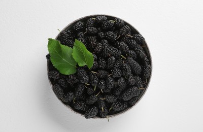 Bowl of delicious ripe black mulberries on white table, top view