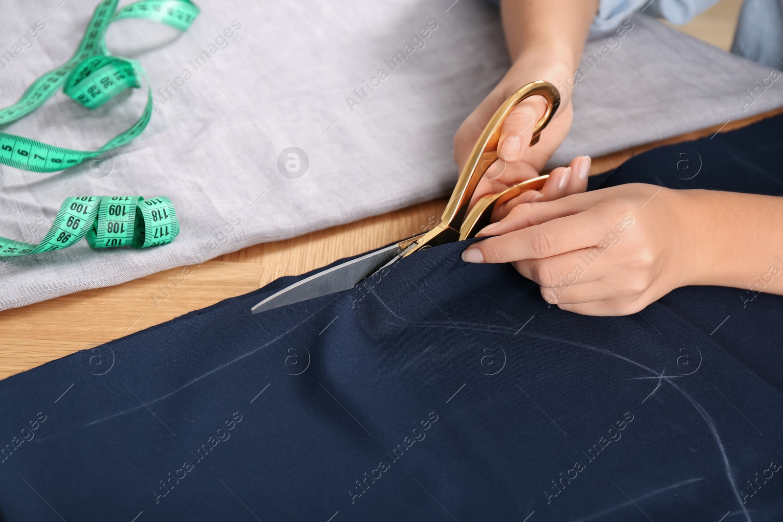 Photo of Woman cutting blue fabric with scissors at wooden table, closeup