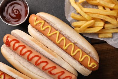 Delicious hot dogs with sauces and French fries on wooden table, top view