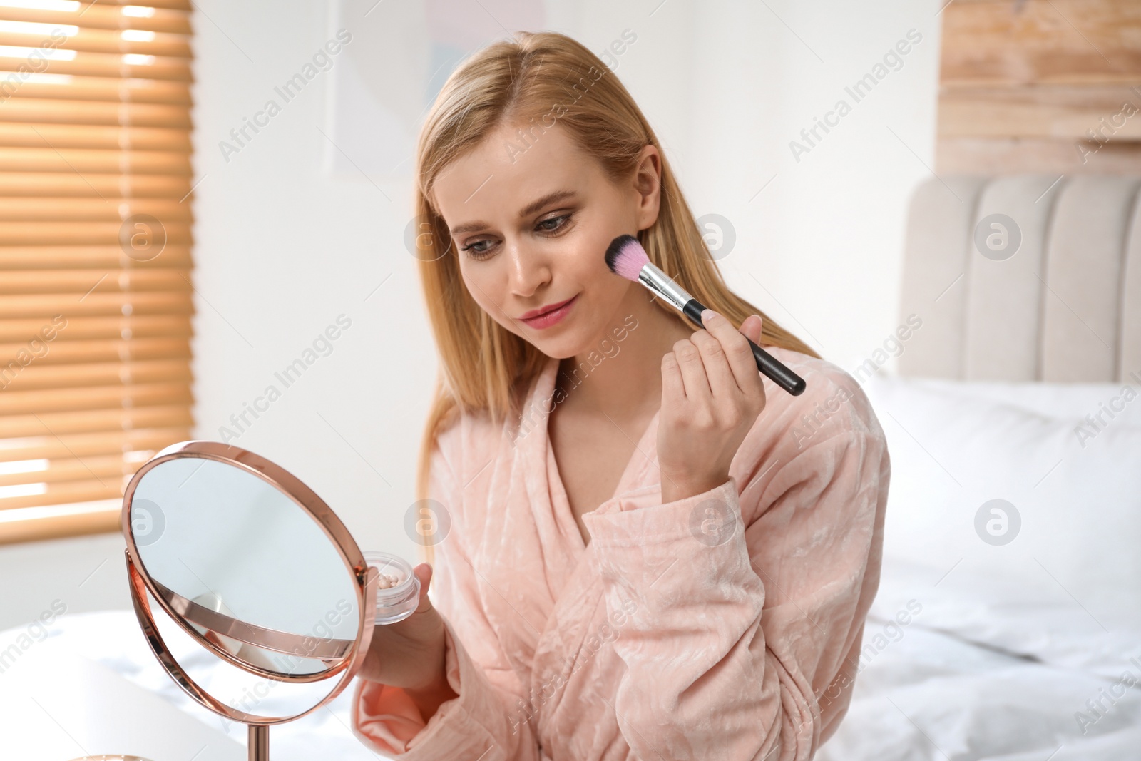 Photo of Beautiful woman with mirror applying makeup in bedroom