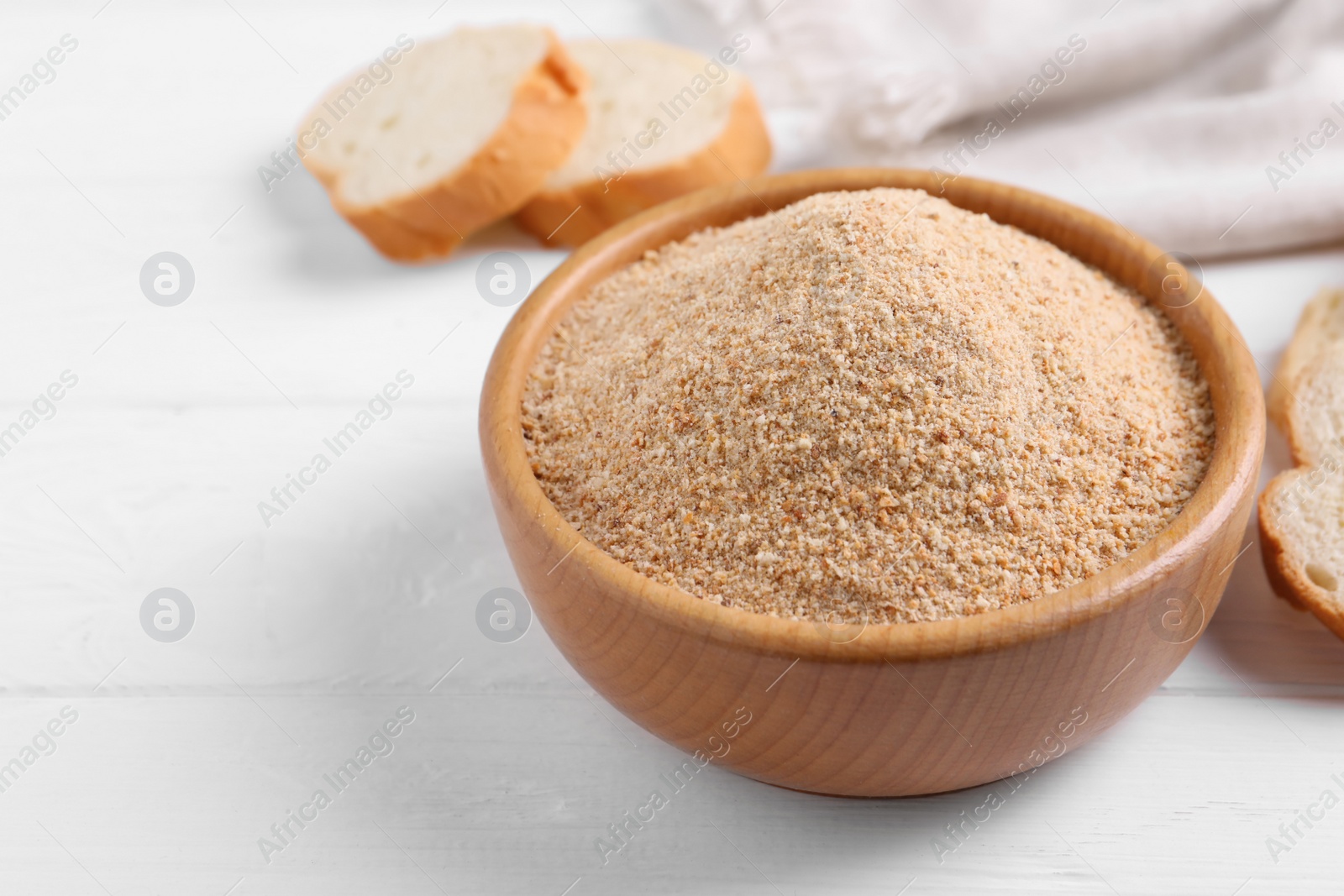 Photo of Fresh breadcrumbs in bowl on white wooden table. Space for text