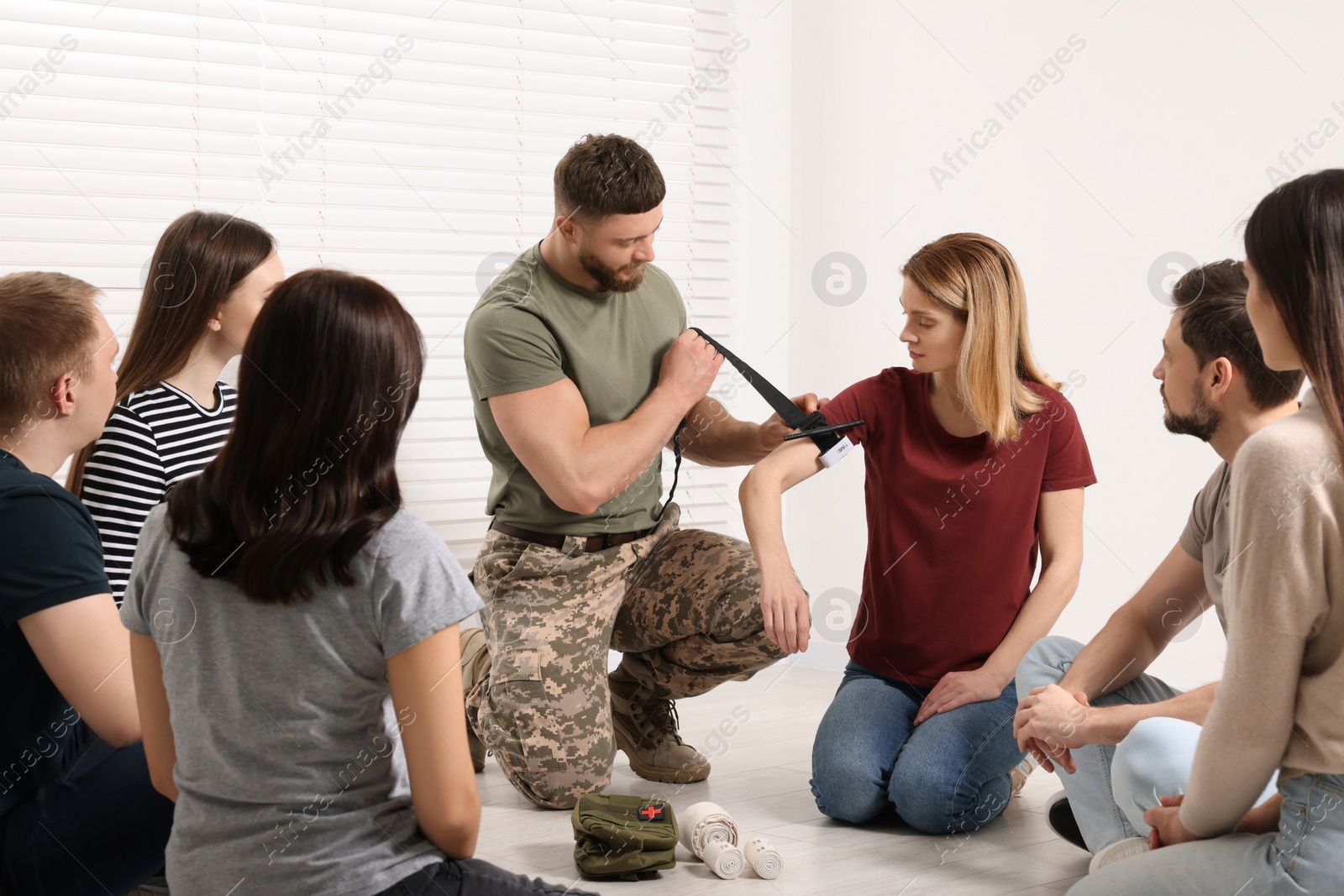 Photo of Soldier in military uniform teaching group of people how to apply medical tourniquet indoors