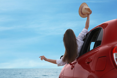 Photo of Happy woman leaning out of car window on beach, space for text. Summer vacation trip
