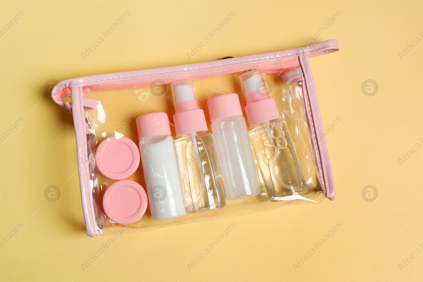 Photo of Cosmetic travel kit in plastic bag on yellow background, top view