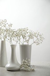Photo of Gypsophila flowers in vases on table against white background