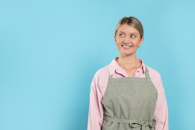 Beautiful young woman in clean apron with pattern on light blue background. Space for text