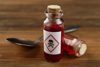 Photo of Vials of poison with spoon on wooden table, closeup