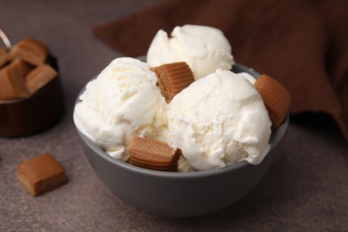 Photo of Scoops of ice cream with caramel candies in bowl on textured table, closeup