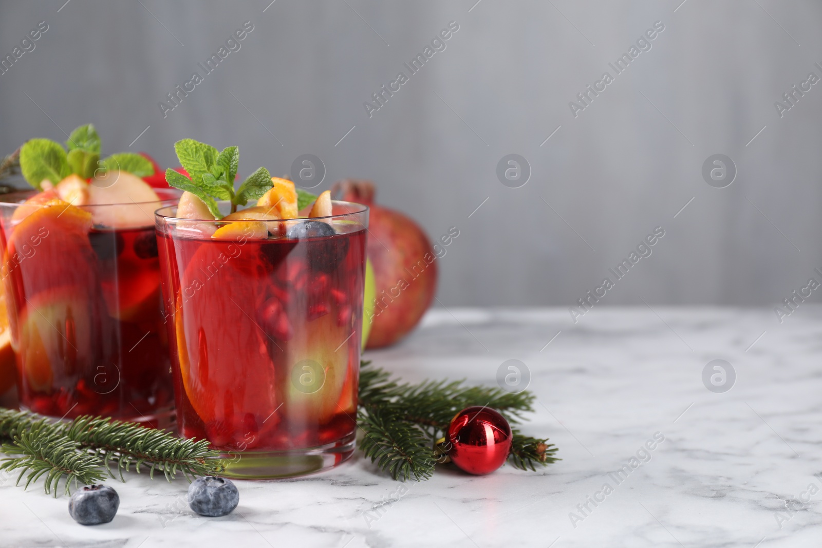 Photo of Aromatic Sangria drink in glasses, ingredients and Christmas decor on white marble table, space for text