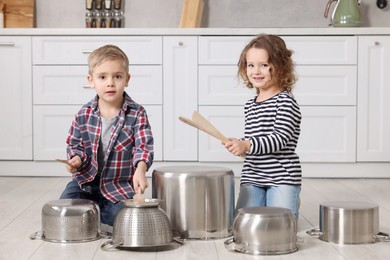 Photo of Little children pretending to play drums on pots in kitchen
