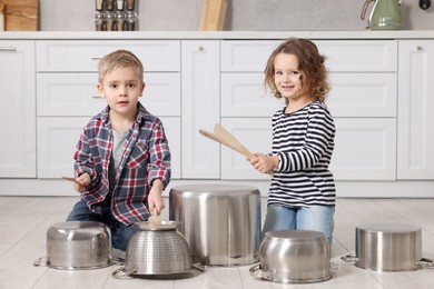 Little children pretending to play drums on pots in kitchen