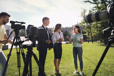 Photo of Professional journalist and operator with video camera taking interview outdoors