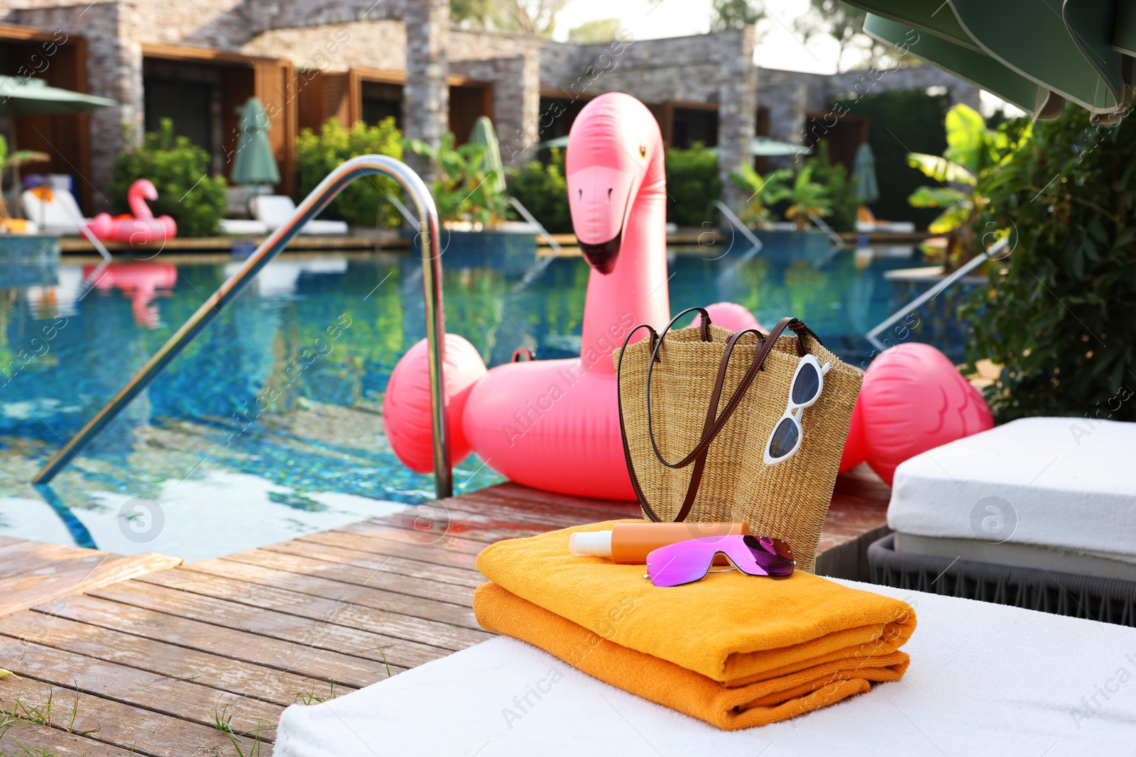 Photo of Wicker bag with beach accessories on sunbed near outdoor swimming pool, space for text. Luxury resort