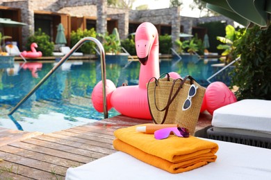 Photo of Wicker bag with beach accessories on sunbed near outdoor swimming pool, space for text. Luxury resort