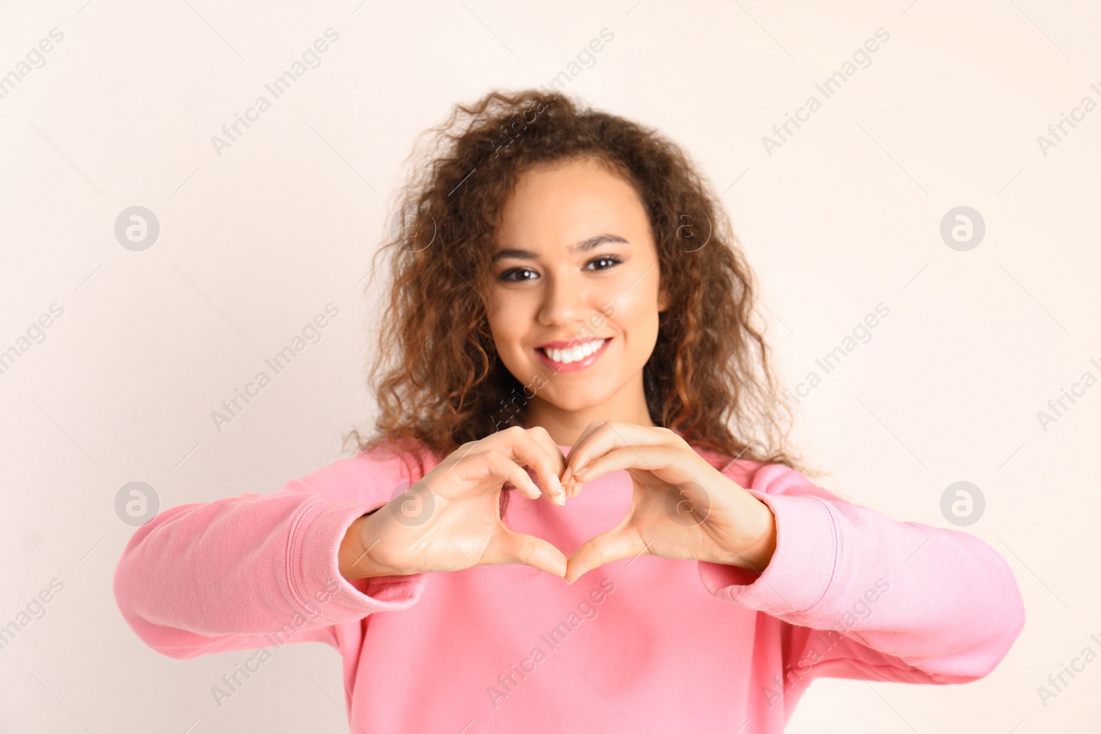 Photo of African-American woman making heart with her hands on white background