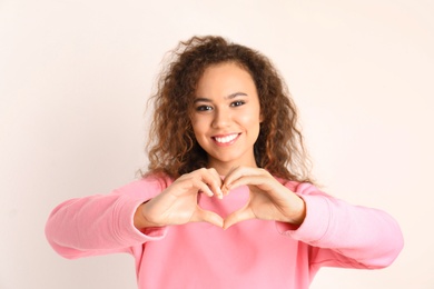 Photo of African-American woman making heart with her hands on white background
