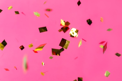 Photo of Shiny golden confetti falling down on pink background