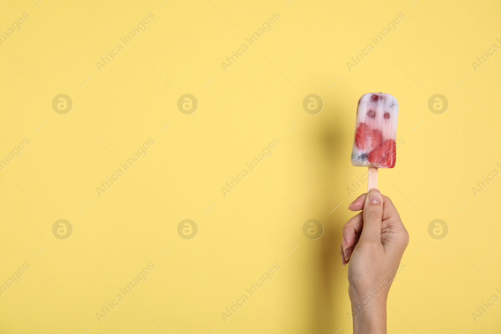 Photo of Woman holding berry popsicle on yellow background, closeup. Space for text