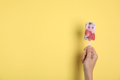 Photo of Woman holding berry popsicle on yellow background, closeup. Space for text