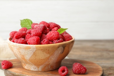 Bowl with delicious ripe raspberries on cutting board against light background, space for text