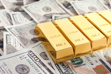 Shiny gold bars on pile of dollar bills