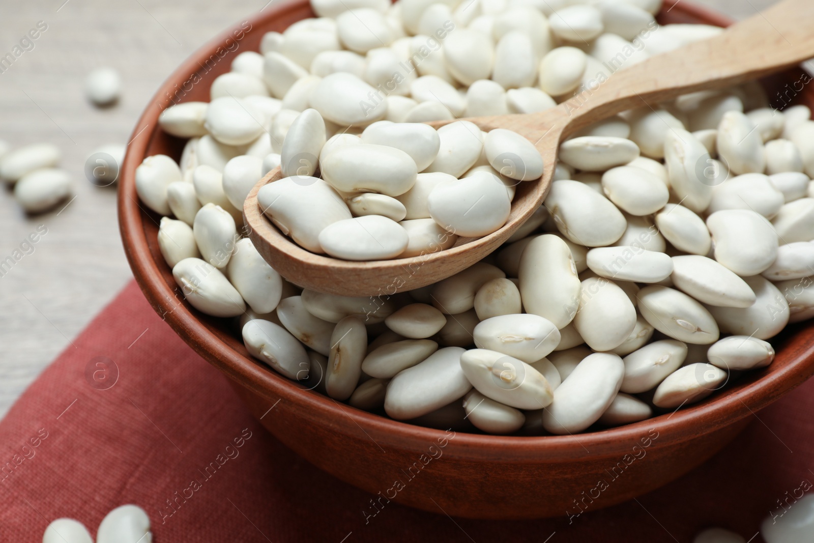 Photo of Raw white beans and spoon in bowl on table, closeup