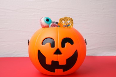Photo of Halloween trick or treat bucket with different sweets on red table
