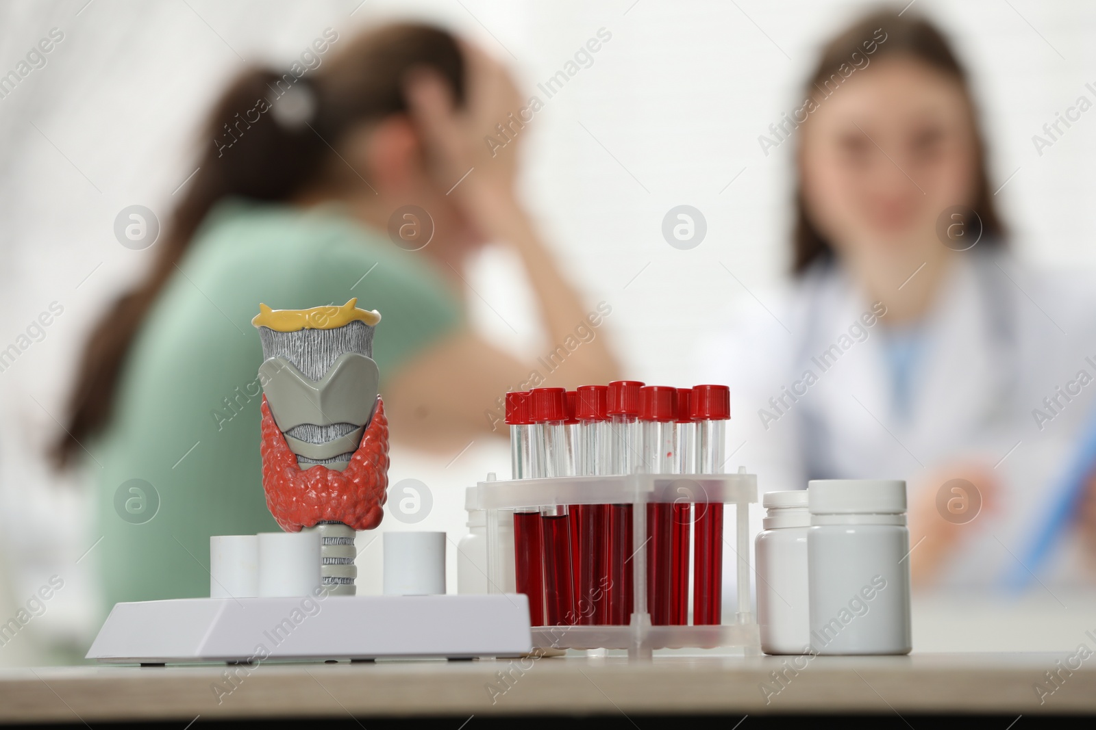 Photo of Endocrinologist examining patient at clinic, focus on model of thyroid gland, pills and blood samples in test tubes