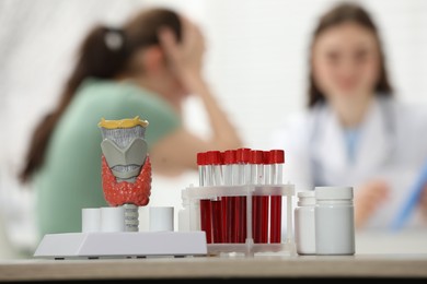 Endocrinologist examining patient at clinic, focus on model of thyroid gland, pills and blood samples in test tubes