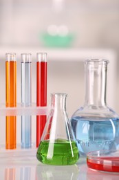 Photo of Laboratory analysis. Glass flasks, Petri dish and test tubes with liquids on white table against blurred background