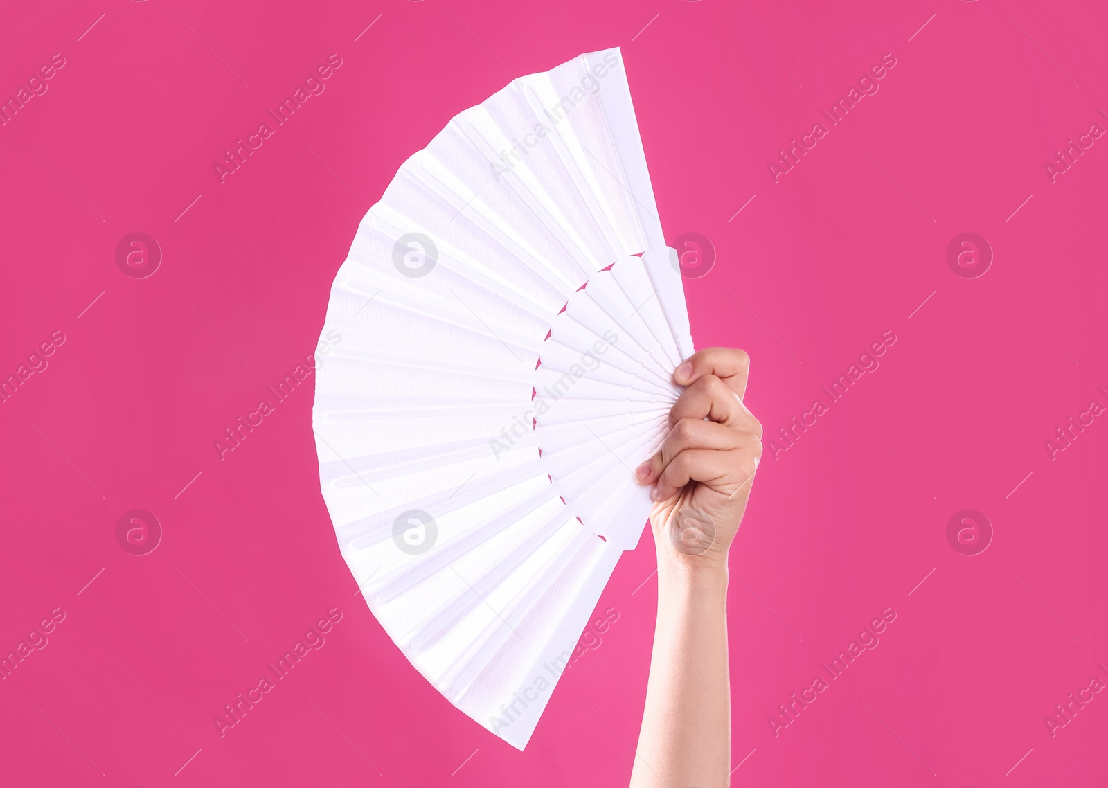 Photo of Woman holding white hand fan on pink background, closeup
