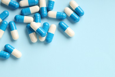 Many antibiotic pills on light blue background, top view. Space for text