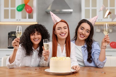 Photo of Happy young women with tasty cake and glassessparkling wine celebrating birthday in kitchen